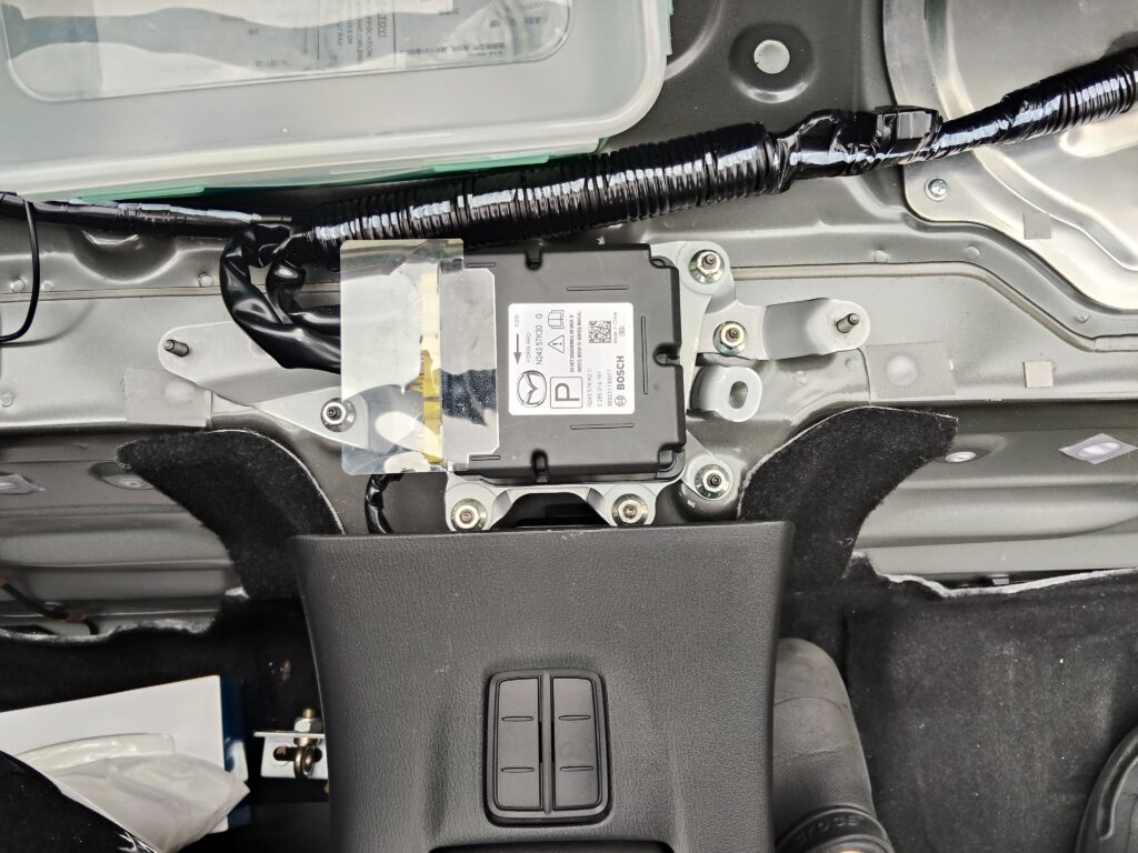 厚見自動車の整備士がND5ロードスター 2号機にSASコントロールモジュール固定金具を取り付けている場面